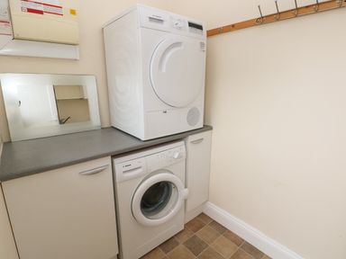 A laundry room with a washing machine and dryer stacked on a countertop and hooks on the wall at Trem Y Morfa in Newport Pembrokeshire