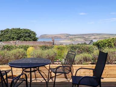 An outdoor patio with a round metal table and chairs overlooking hedges rooftops and coastal hills at Trem Y Morfa in Newport Pembrokeshire