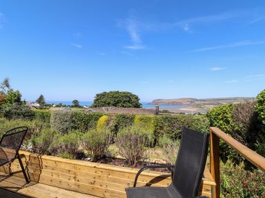 A wooden deck with chairs overlooking hedges houses and a beach at Trem Y Morfa in Newport Pembrokeshire