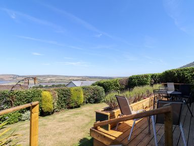 A garden with a wooden deck and outdoor furniture overlooking a hedge and countryside at Trem Y Morfa in Newport Pembrokeshire