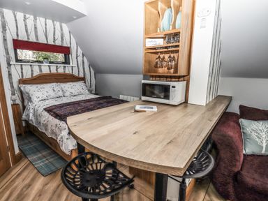 A small bedroom with a double bed beside a wooden counter with stools microwave and wooden shelves at Silver Birch Lodge in Misterton