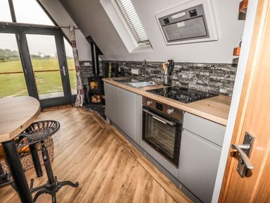 A kitchen with a stove oven sink wood burning stove and bar stools at Silver Birch Lodge in Misterton