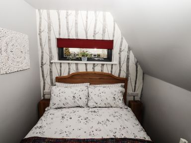 A bedroom with a wooden bed and floral bedding under a window with a red blind at Silver Birch Lodge in Misterton