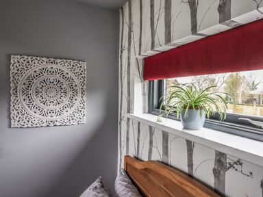 A bedroom corner with a wooden headboard a potted plant on the windowsill red window blind and decorative wall art at Silver Birch Lodge in Misterton