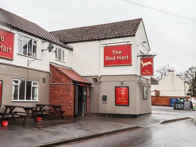 Exterior view of The Red Hart pub with outdoor benches on a wet pavement