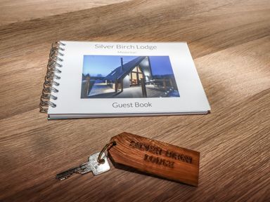 A guest book and a key with a wooden keychain on a wooden surface at Silver Birch Lodge in Misterton
