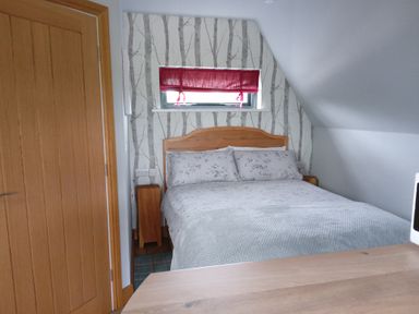 A bedroom with a wooden bed frame and floral bedding under a window with a red blind at Silver Birch Lodge in Misterton