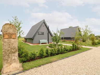 Two triangular lodges with gray roofs and walls with a green bench outside one and a gravel path leading to them at Silver Birch Lodge in Misterton