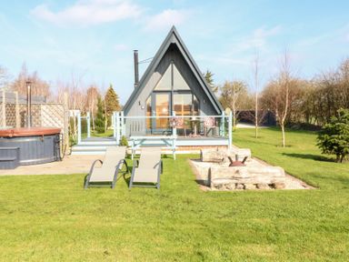 A garden with two lounge chairs a fire pit a hot tub and a small A-frame cabin with a porch at Silver Birch Lodge in Misterton