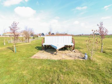 An outdoor grassy area with a white wooden bench with large wheels and small trees around at Silver Birch Lodge in Misterton