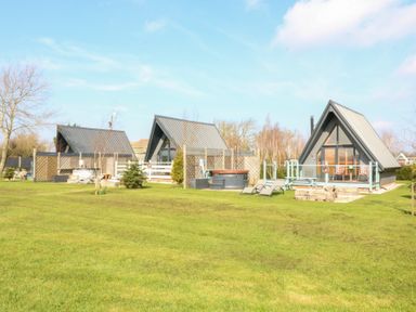 Three a-frame cabins on a grassy lawn with outdoor seating and trees in the background at Silver Birch Lodge in Misterton