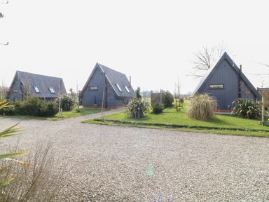 Three A-frame houses with dark roofs and windows surrounded by grass and shrubs with a gravel driveway in front at Silver Birch Lodge in Misterton
