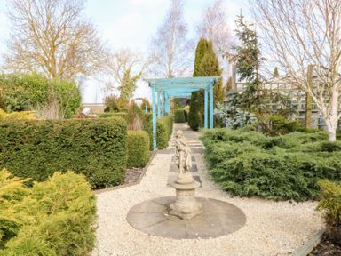 A garden pathway with a statue and blue pergola surrounded by hedges and trees at Silver Birch Lodge in Misterton