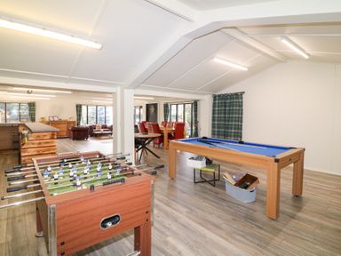 A game room with a foosball table and a pool table with dining area and seating in the background at Silver Birch Lodge in Misterton