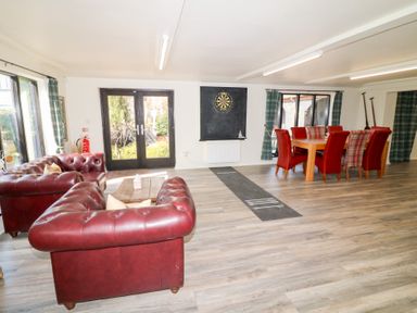 A living room with red leather sofas a wooden table a dining table with red and plaid chairs dartboard and large windows at Silver Birch Lodge in Misterton