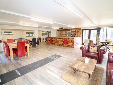 A large room with red and black chairs around wooden tables a wooden bar area and leather armchairs at Silver Birch Lodge in Misterton