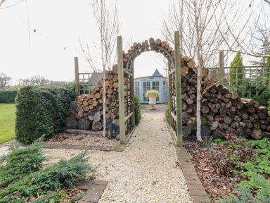 A garden path with a wood log archway and a shed in the background at Silver Birch Lodge in Misterton