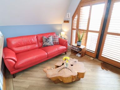A living room with a red sofa wooden coffee table and window shutters at Silver Birch Lodge in Misterton