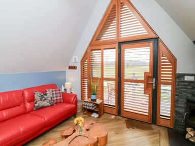 A living room with a red leather sofa pillows wooden coffee table and wooden shutters at Silver Birch Lodge in Misterton