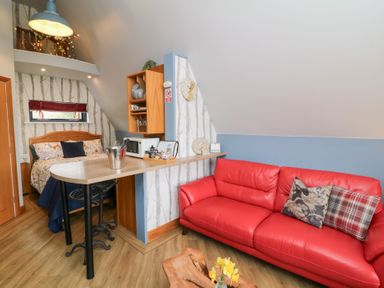 A room with a red sofa, wooden table, bed, and kitchenette at Silver Birch Lodge in Misterton