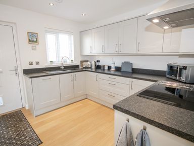 A kitchen with white cabinets black countertops a stove a microwave a toaster and a window at 14 Parc Delfryn Brynteg near Benllech