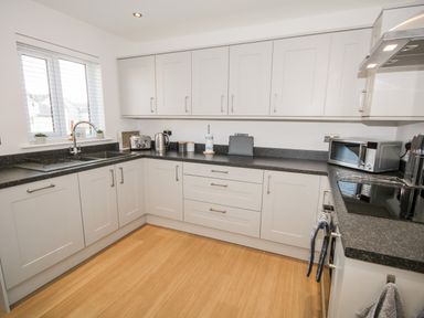 A kitchen with white cabinets black countertops a sink toaster kettle microwave and electric stove at 14 Parc Delfryn in Brynteg near Benllech