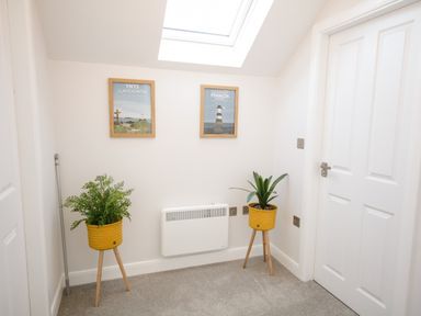 A small corner room with two plants in yellow pots on wooden stands and two framed pictures on the wall at 14 Parc Delfryn in Brynteg near Benllech