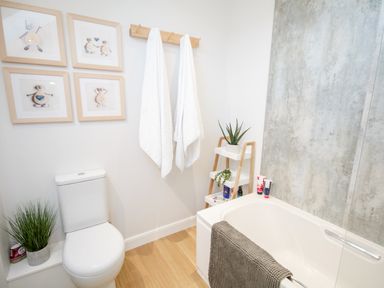 A bathroom with a toilet plants towels on a rack and a bathtub with a gray towel at 14 Parc Delfryn in Brynteg near Benllech
