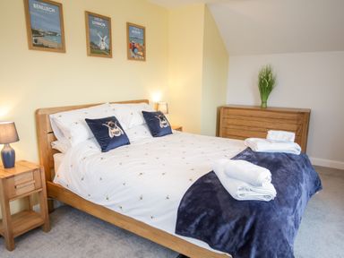 A bedroom with a wooden bed and nightstands with lamps and framed pictures on the wall at 14 Parc Delfryn Brynteg near Benllech