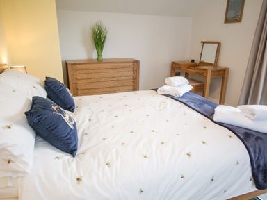 A bedroom with a bed with bee patterned bedding and blue pillows next to a wooden dresser and dressing table at 14 Parc Delfryn Brynteg near Benllech