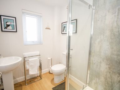 A bathroom with a shower, toilet, sink, towel rack, and window at 14 Parc Delfryn Brynteg near Benllech
