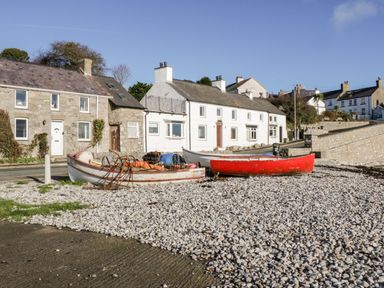 Three boats on a pebble beach in front of stone and white houses at 14 Parc Delfryn Brynteg near Benllech