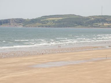 A wide sandy beach with a few people walking near the shore and hills in the background at 14 Parc Delfryn Brynteg near Benllech