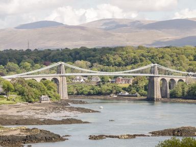A suspension bridge over water with houses and trees in the background and hills beyond at 14 Parc Delfryn Brynteg near Benllech