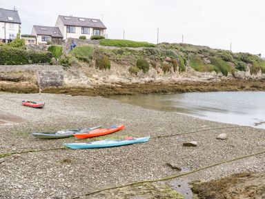 A rocky shoreline with kayaks and houses on a cliff at 14 Parc Delfryn in Brynteg near Benllech