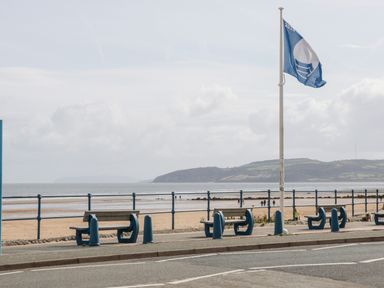 A seaside promenade with benches railings a flagpole and a sandy beach at 14 Parc Delfryn in Brynteg near Benllech