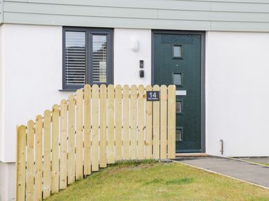 A black front door and window behind a wooden fence with a house number 14 Parc Delfryn Brynteg near Benllech