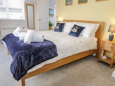 A bedroom with a wooden bed with white bedding and blue pillows with bee designs at 14 Parc Delfryn Brynteg near Benllech