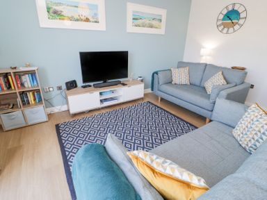 A living room with two blue sofas a patterned rug a TV on a cabinet and bookshelves at 14 Parc Delfryn Brynteg near Benllech