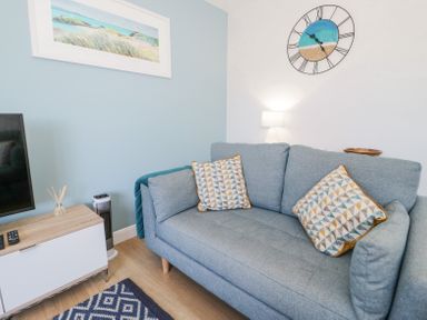 A living room with a blue sofa and patterned cushions a wall clock and a framed picture at 14 Parc Delfryn in Brynteg near Benllech