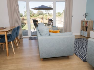 A living room with a light blue sofa facing a glass door opening to a patio with chairs and an umbrella at 14 Parc Delfryn Brynteg near Benllech