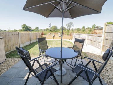 An outdoor patio with a glass table and four black chairs under an umbrella at 14 Parc Delfryn in Brynteg near Benllech