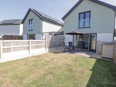 A backyard with patio furniture and umbrella next to a modern two-story house with a fenced lawn at 14 Parc Delfryn in Brynteg near Benllech
