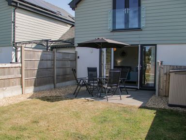 A backyard with a patio table umbrella and chairs next to a house at 14 Parc Delfryn in Brynteg near Benllech