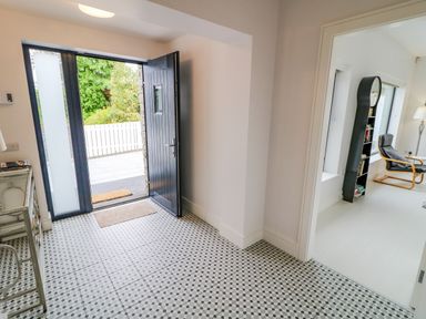 An entryway with an open black door and patterned tile floor leading to a room with a chair bookshelf and floor lamp at Wee Andy's in Slavary near Buncrana County Donegal