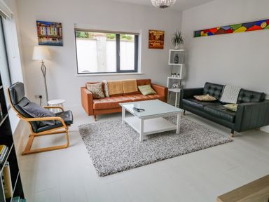 A living room with two leather sofas a black armchair a white coffee table a floor lamp and wall art at Wee Andy's Slavary near Buncrana County Donegal