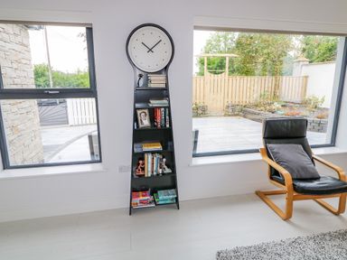A room with a black clock bookshelf between two windows and a black leather chair with a gray pillow at Wee Andy's in Slavary near Buncrana County Donegal