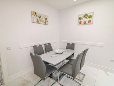 A dining area with a glass table and six gray chairs with artwork on the walls at Wee Andy's in Slavary near Buncrana County Donegal
