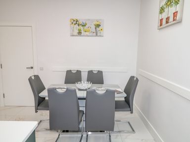 A dining area with six gray chairs around a rectangular glass table and flower paintings on white walls at Wee Andy's in Slavary near Buncrana County Donegal