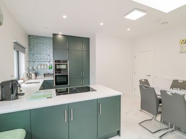 A kitchen with green cabinets white countertops a dining table with gray chairs at Wee Andy's in Slavary near Buncrana County Donegal